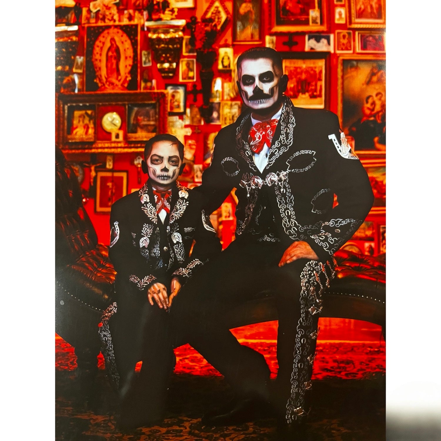 Padre e hijo vestidos con trajes de charro negros tradicionales frente a un fondo decorado mexicano, atuendo elegante para celebraciones culturales.