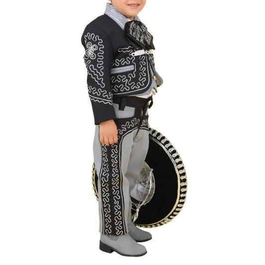 A young boy wearing a traditional charro suit with black and white embroidery, including a jacket, pants, a vest, shirt, bow tie, sombrero, and belt.